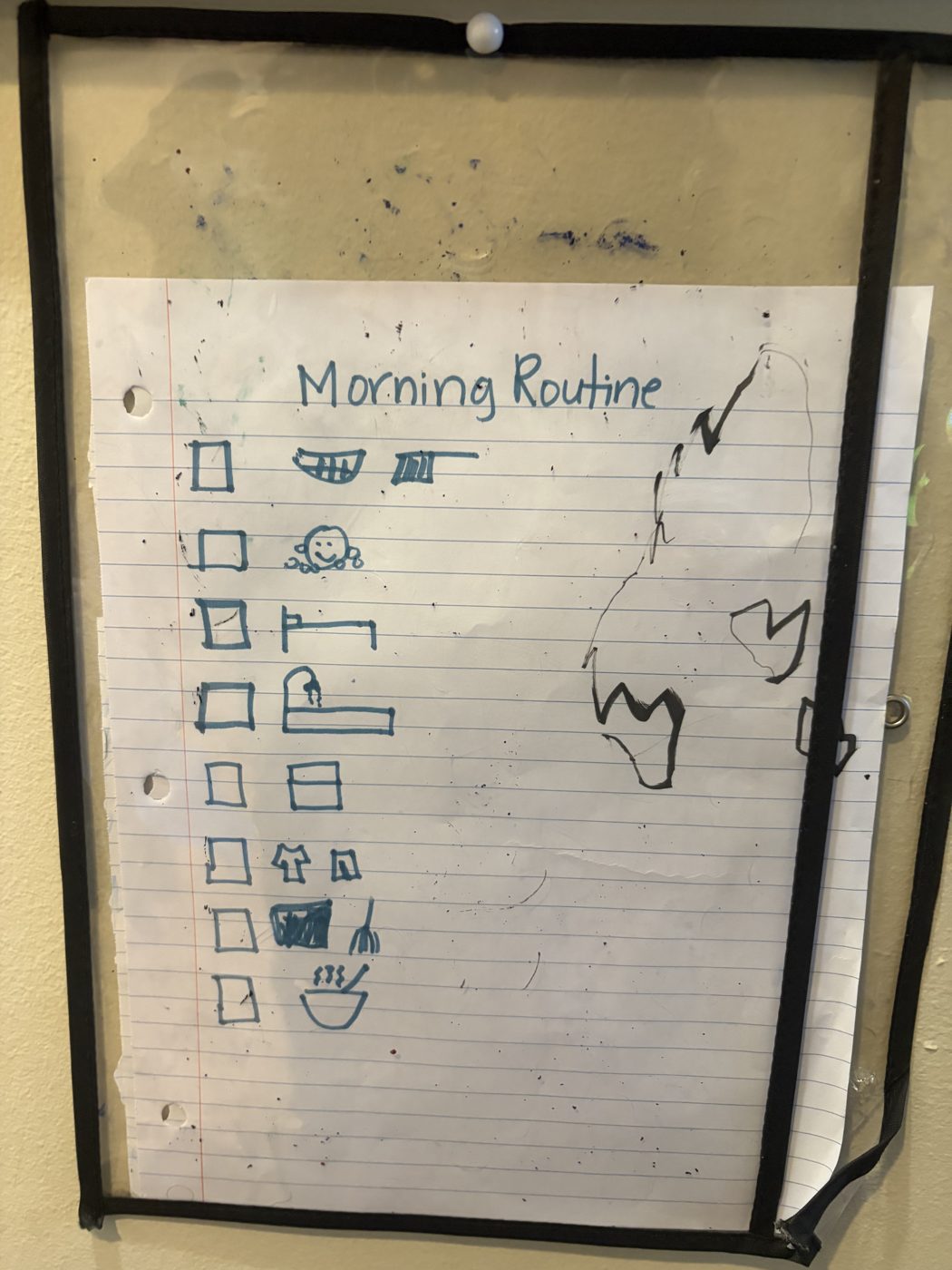 A hand-drawn Morning Routine checklist on lined paper in a clear sleeve, with eight checkboxes and a simple drawing for each step, including brushing teeth, making the bed, getting dressed, and eating breakfast.